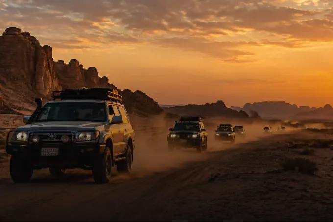 Vehicle convoy crossing the desert at sunset